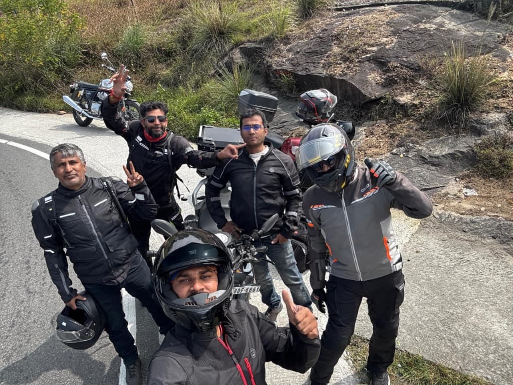 Group photo of riders posing along a winding mountain highway